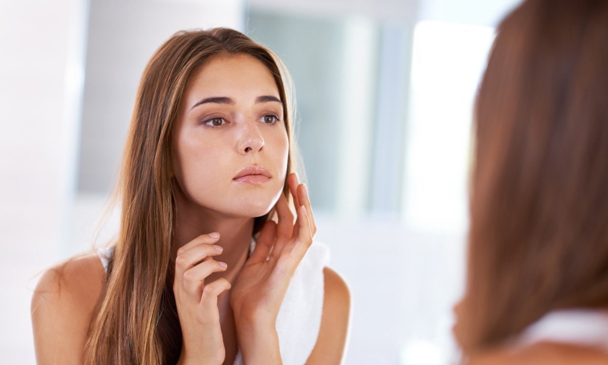 زنی در مقابل آیینه که به پوست خود نگاه می کند- درمان خانگی لک های پوستی