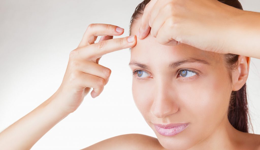 زنی با چشمان آبی در حال دست زدن به جوش صورت- جوش زدن صورت